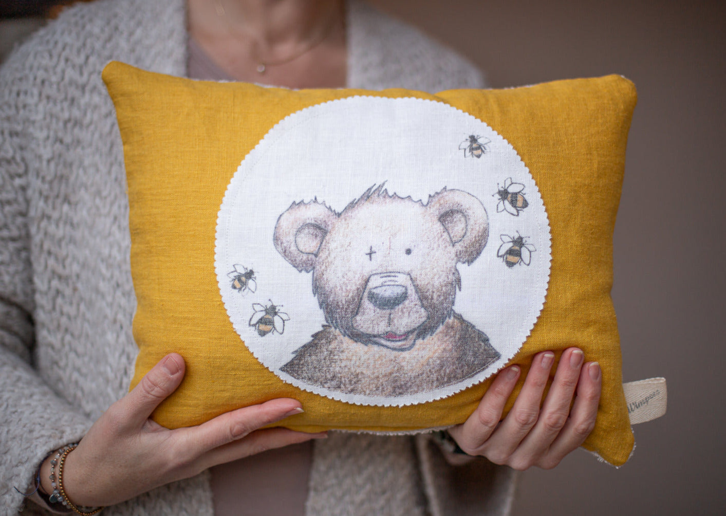 Zirbenkissen aus Leinen Farbe Senf mit Teddykopf und Bienchen auf weißem Patch.