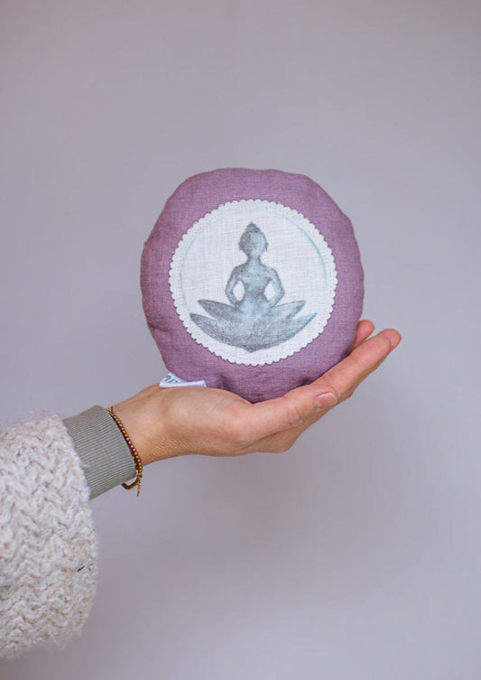 Rundes Dinkelkissen aus Leinen Farbe Lavendel mit Buddha auf Lotusbluete auf weißem Patch.